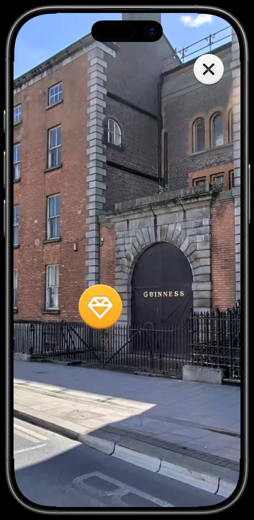 The AR lens on an iPhone: the camera view fills the screen, a Dublin street with the old Guinness gate, and an orange gem badge marking a discovered Hidden Sight, with a close button in the corner.